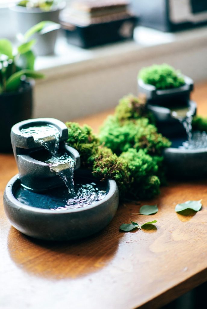 Compact zen water feature with gentle cascading flow over moss-covered rocks on wooden desk, perfect calming desk decoration accent.